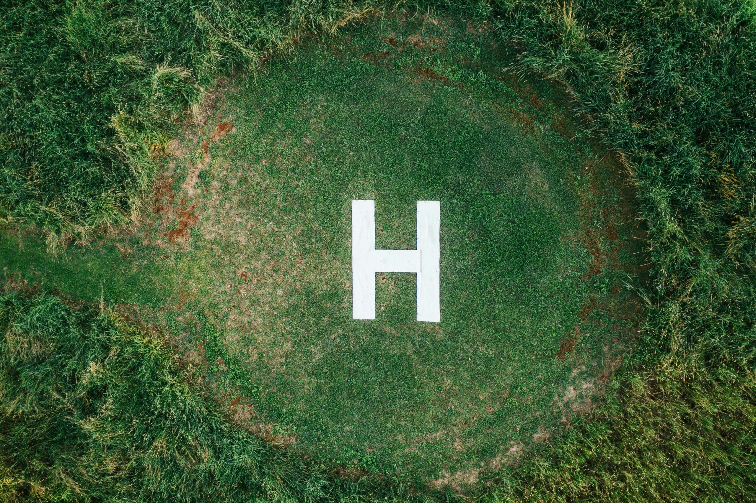 Aerial shot of a grass heliport with a marked 'H' for helicopter landing, located in Dalwood, NSW, Australia.